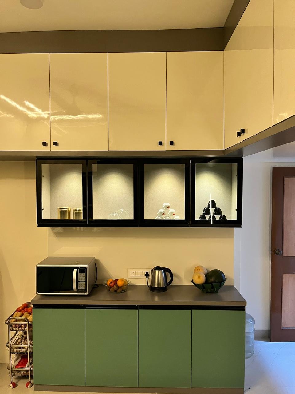 Compact modular kitchen in cream and sage green with lit glass display cabinets