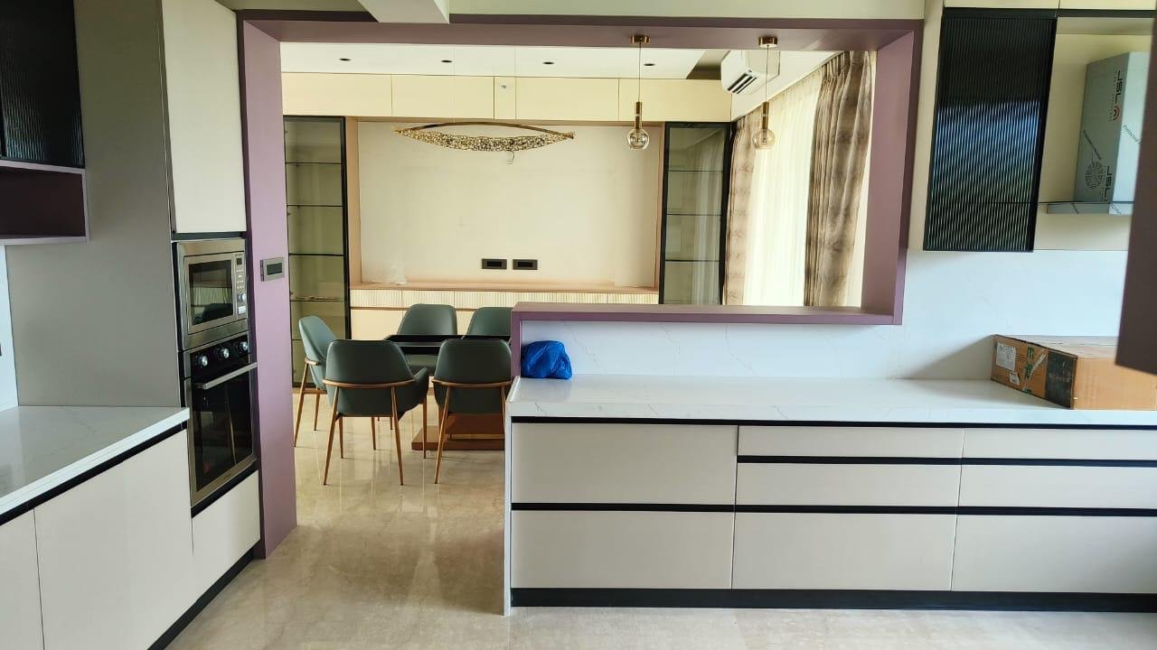 Open modular kitchen in white and mauve with a breakfast counter overlooking the dining area