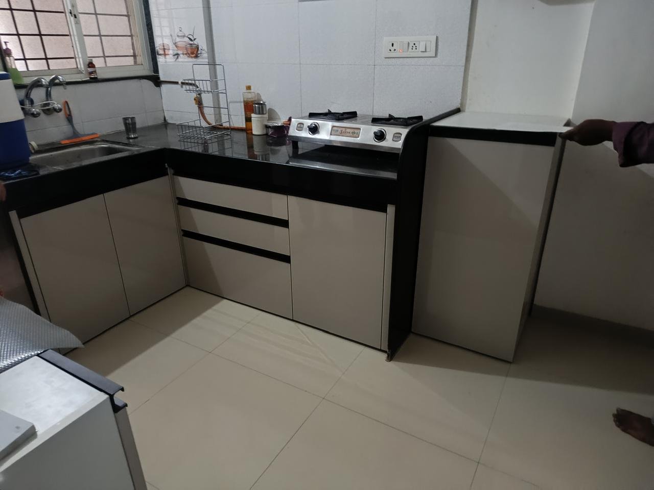 L-shaped modular kitchen in beige with a black countertop and dark glass cabinets