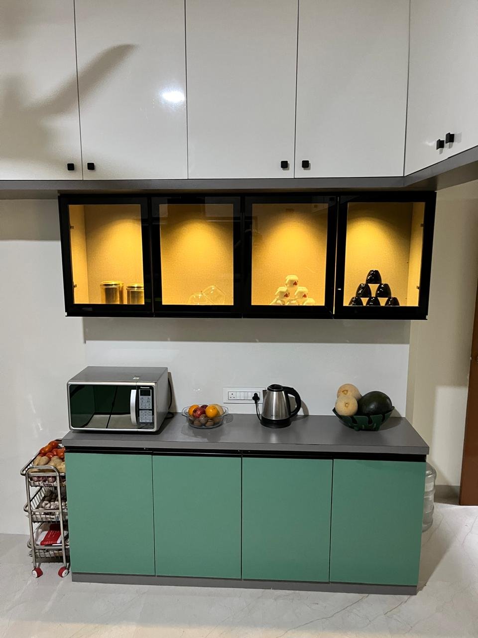 Kitchen counter in white and sage green with lit black glass display cabinets