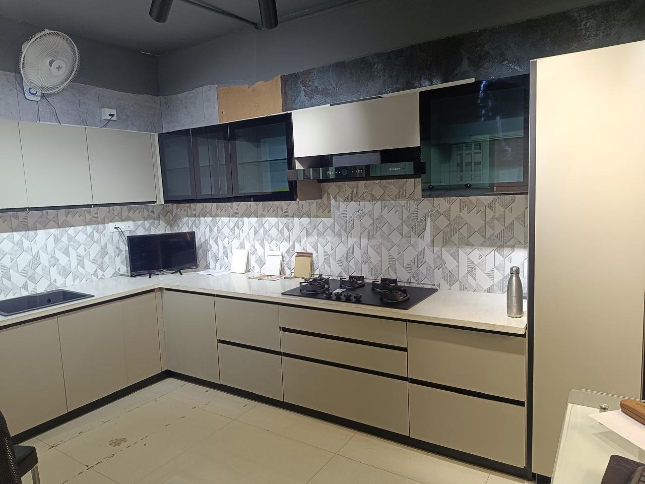 L-shaped modular kitchen in beige with black glass wall cabinets and a patterned backsplash
