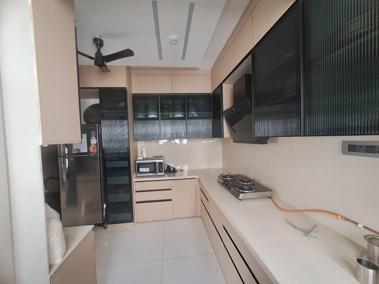 L-shaped modular kitchen in beige with black fluted glass cabinets